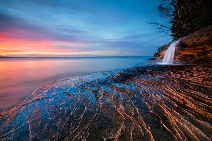 Waterfall cascading over rocks into a lake at sunset