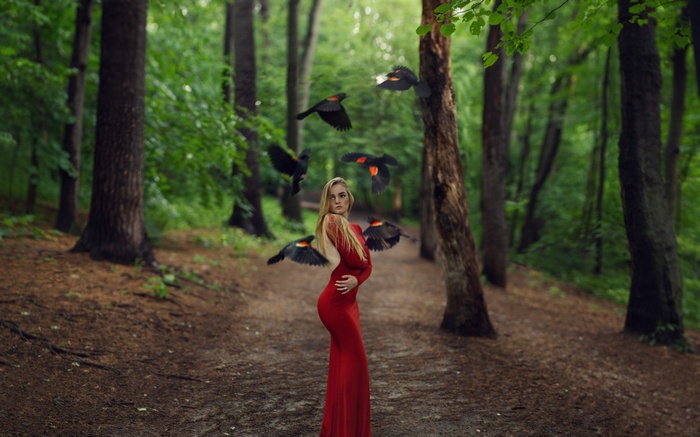 Woman in red dress surrounded by birds in a forest
