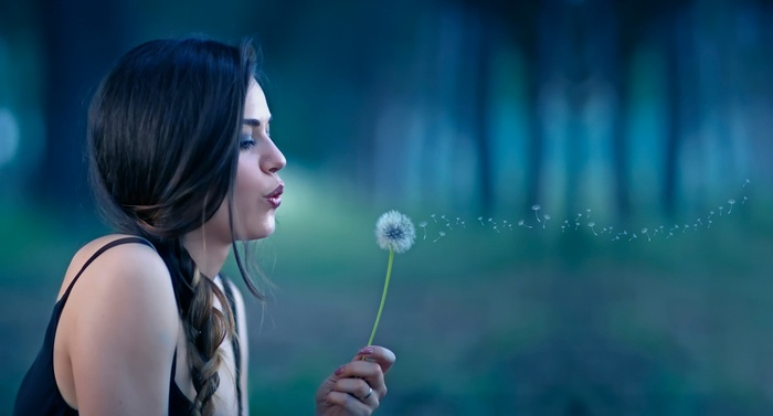 Woman blowing dandelion seeds in a forest