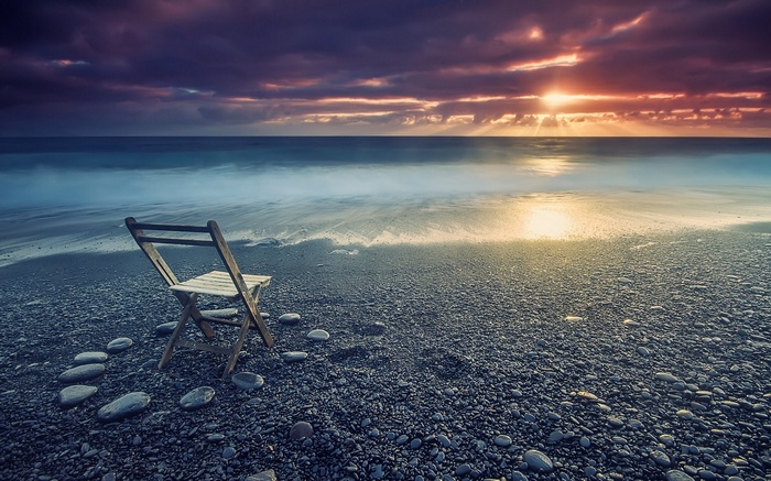 Wooden chair on a pebble beach at sunset