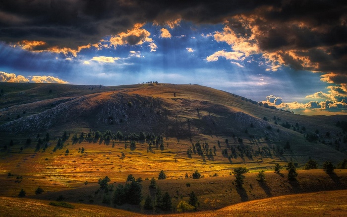 Sun rays breaking through clouds over a mountainous landscape