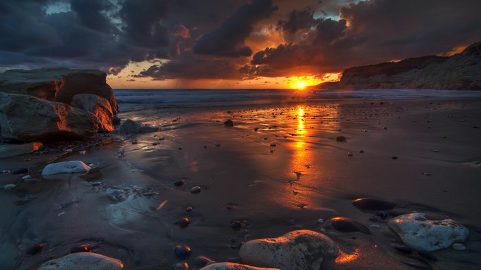 Sunset over a rocky beach with waves and clouds