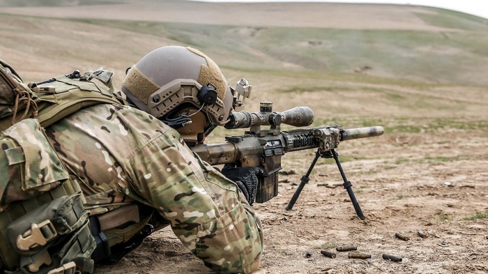Soldier aiming a sniper rifle in a desert landscape