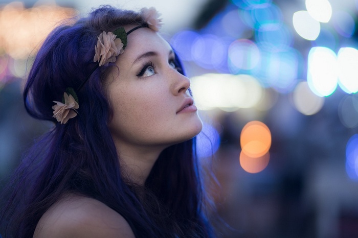 Woman with purple dyed hair and flower crown looking up