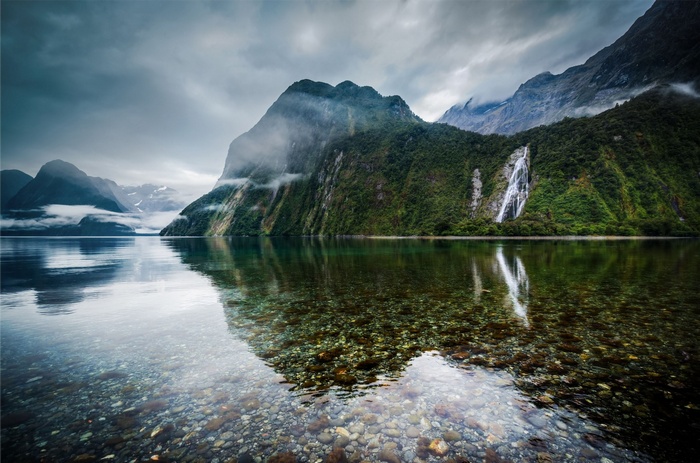 Waterfall cascading down a misty mountain into a clear lake
