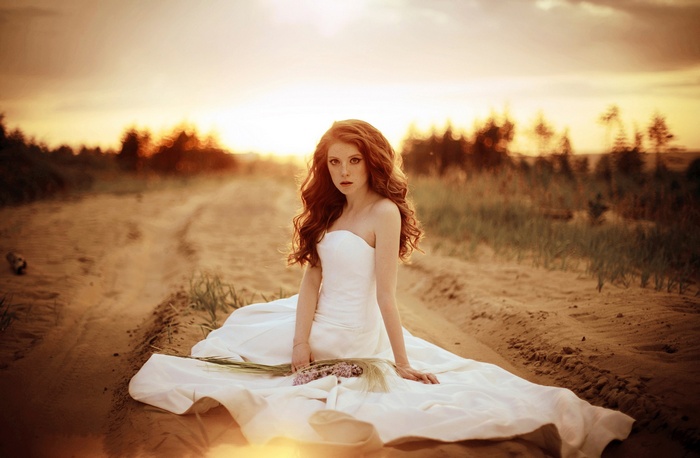 Redhead woman in white dress sitting in a field