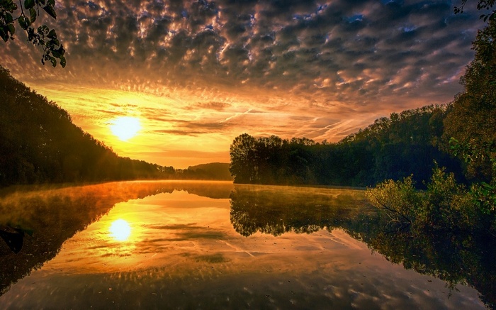 Sunrise over a misty lake with forested hills