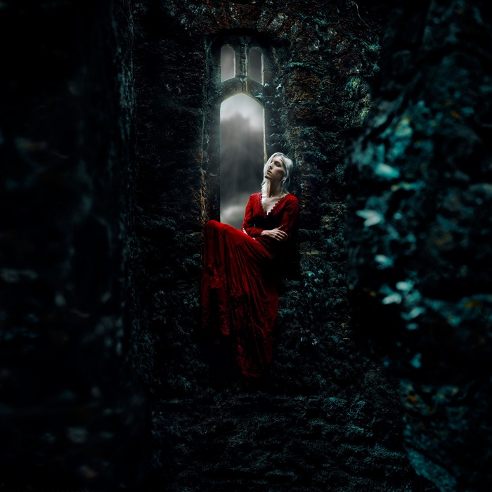Woman in red dress sitting in a gothic window