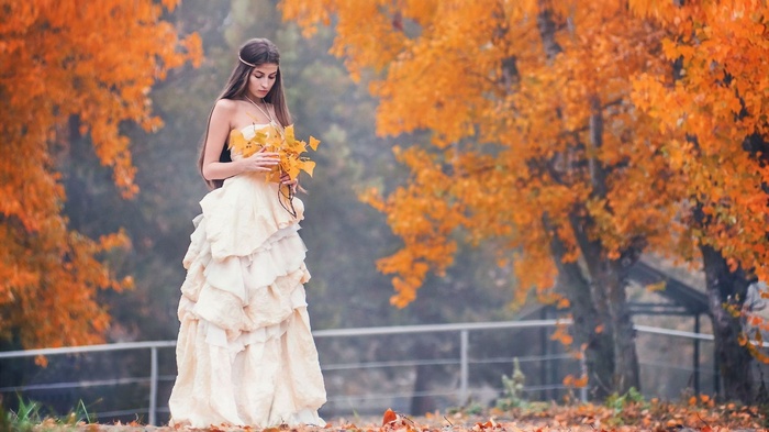 Woman in a white dress holding autumn leaves