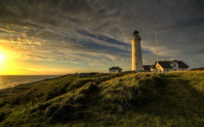 Lighthouse and houses on a grassy hill at sunset