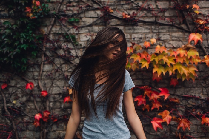 Woman with long brown hair in front of a brick wall with ivy