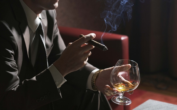 Man in suit smoking cigar and drinking brandy