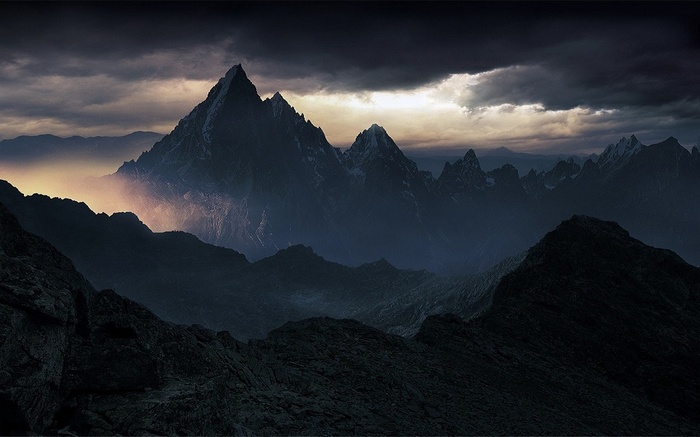 Dark mountains shrouded in mist under stormy clouds