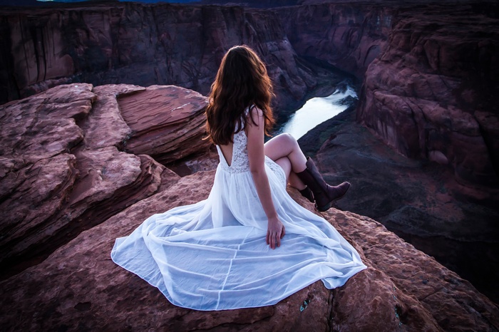 Woman in white dress sitting on cliff edge overlooking canyon