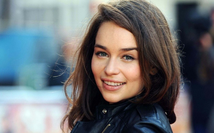 Emilia Clarke smiling outdoors wearing a leather jacket