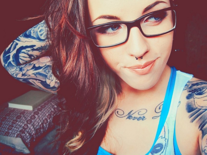 Woman with tattoos and glasses looking away