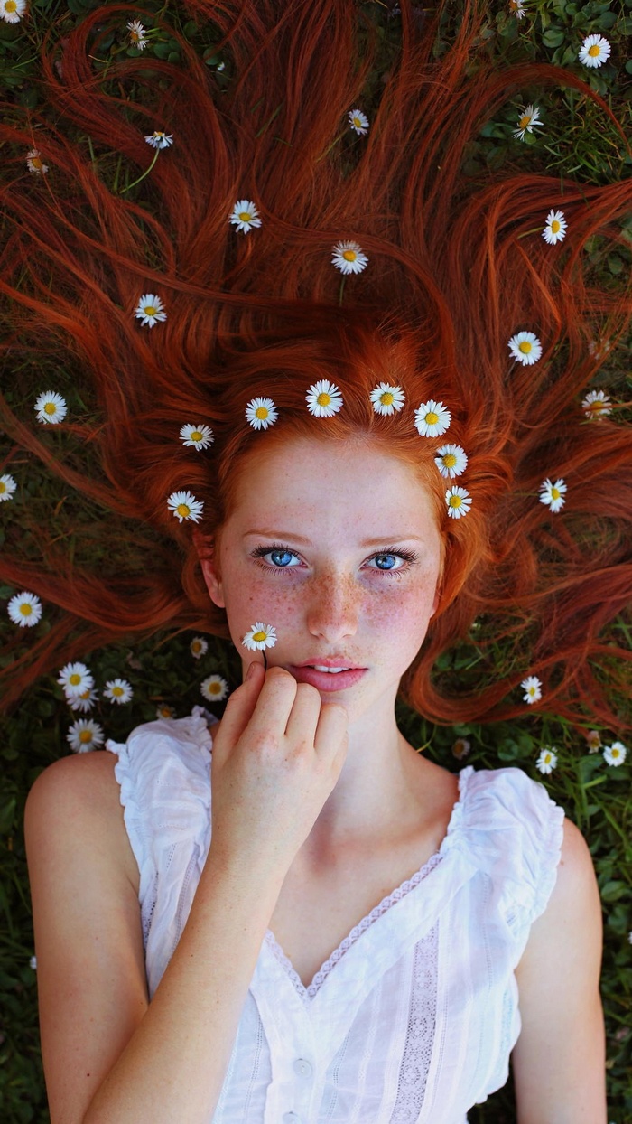 Redhead woman with blue eyes lying in grass with daisies