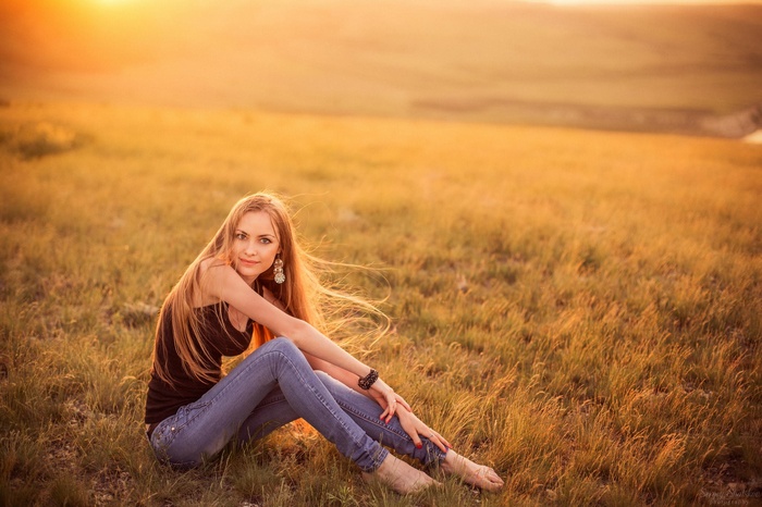 Woman with blonde hair sitting in a grassy field at sunset