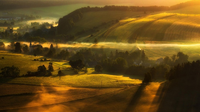 Misty valley with golden sunrise over fields and village