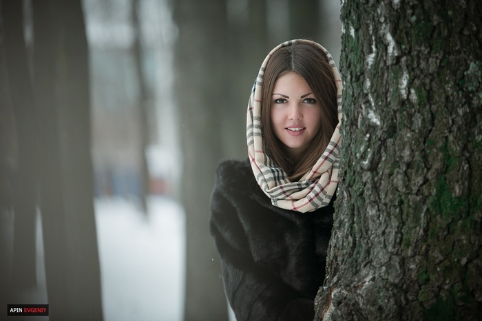 Woman in fur coat and scarf behind a tree