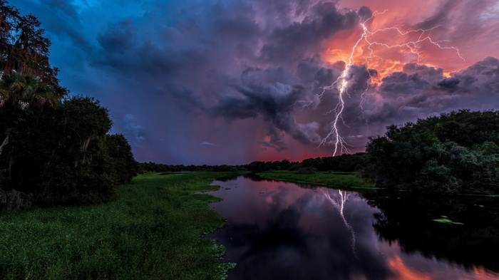 Lightning strikes over a river in Florida during a storm at sunset