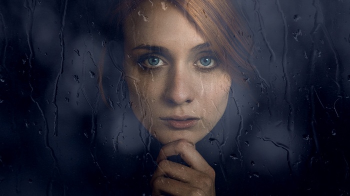 Woman with red hair and blue eyes behind wet glass