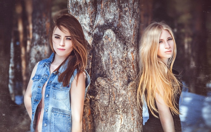 Two women leaning against a tree in a forest