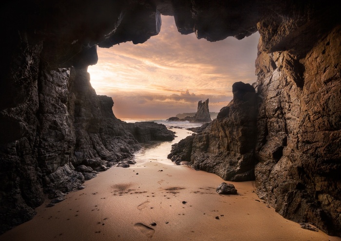 Cave entrance overlooking a rocky beach at sunset