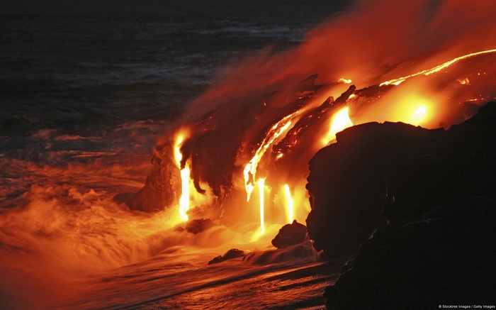 Lava flows into the ocean at night