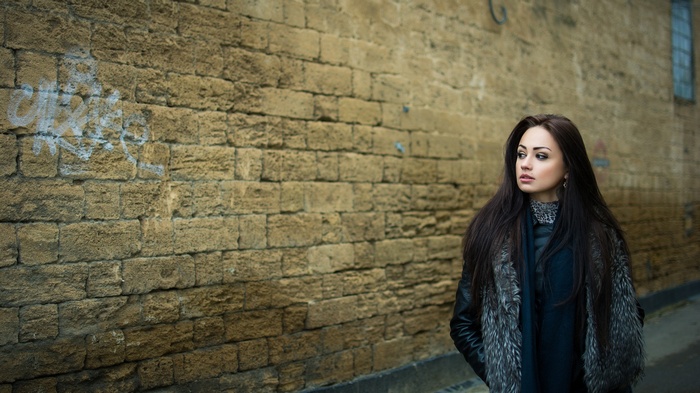 Woman in fur coat standing by a brick wall