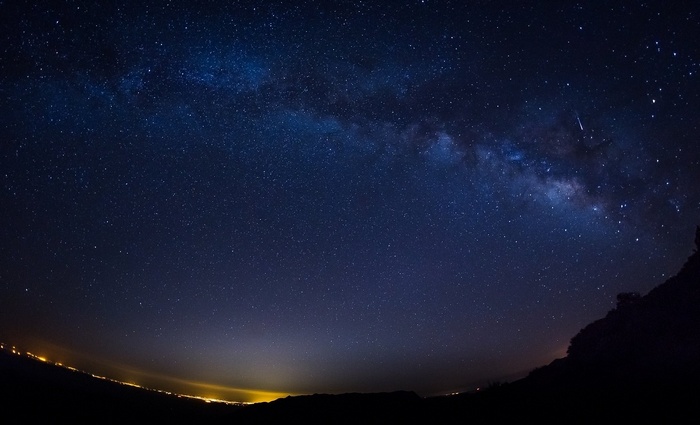 Starry night sky over a dark landscape with city lights