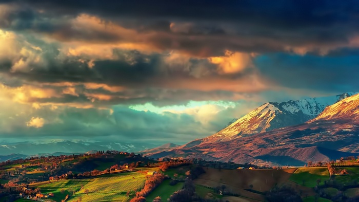 Dramatic clouds over rolling hills and snow-capped mountains