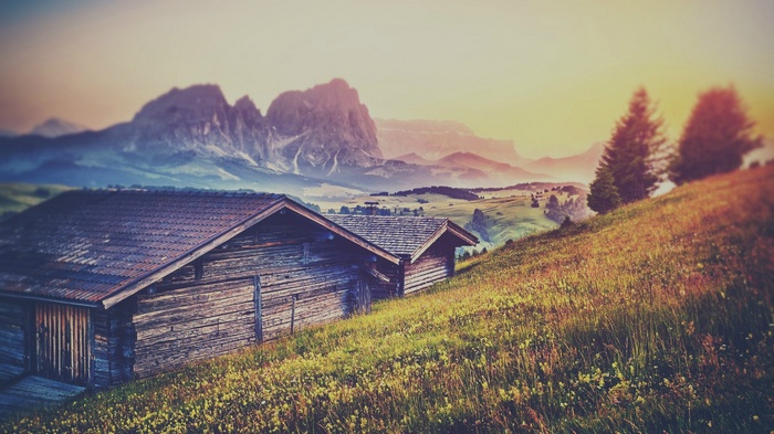 Wooden barns on a grassy hillside with mountains in the background