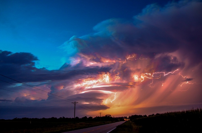 Lightning strikes through colorful storm clouds over a road