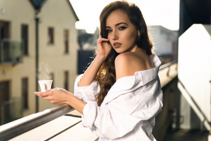 Woman in white shirt holding a coffee cup on a balcony