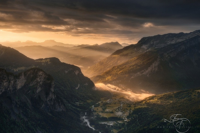 Sunlight streams through a mountain valley with a village