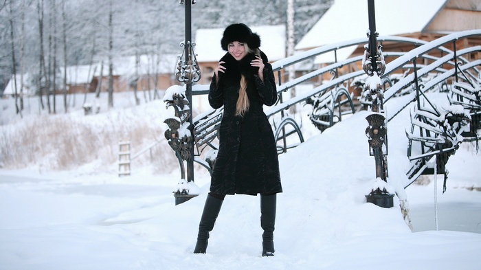 Woman in black coat and fur hat on a snowy bridge