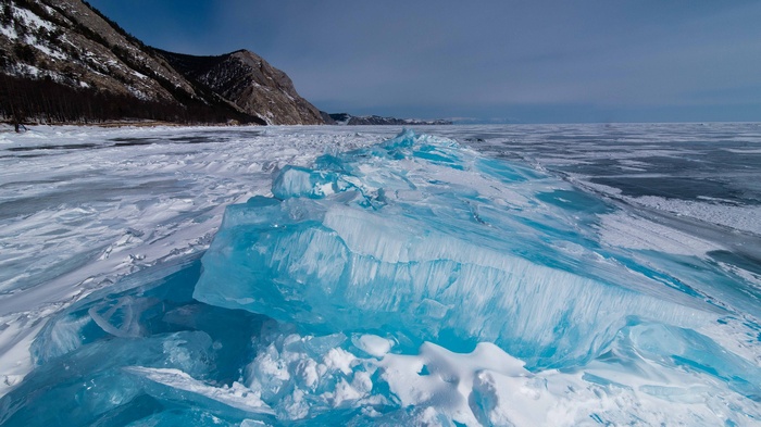 Blue ice formations on a frozen lake with mountains