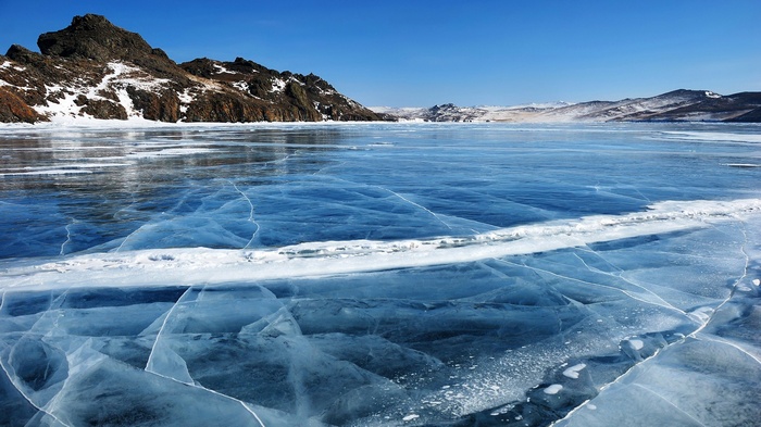 Frozen lake with mountains under a clear blue sky