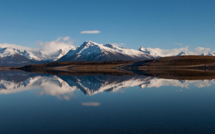 Snowy mountains reflected in a calm lake under a blue sky