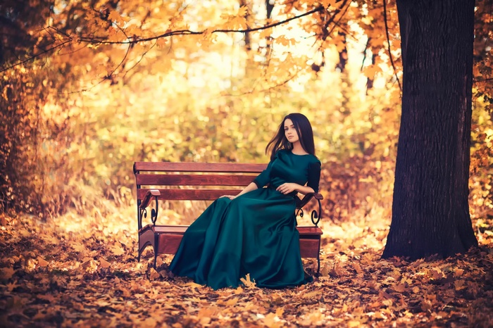 Woman in a green dress sitting on a park bench in autumn