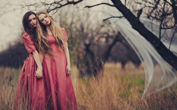 Two women in pink dresses holding hands in nature
