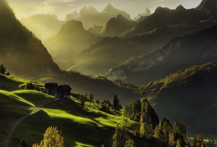 Sunlight over Swiss Alps valley with cabins and forest