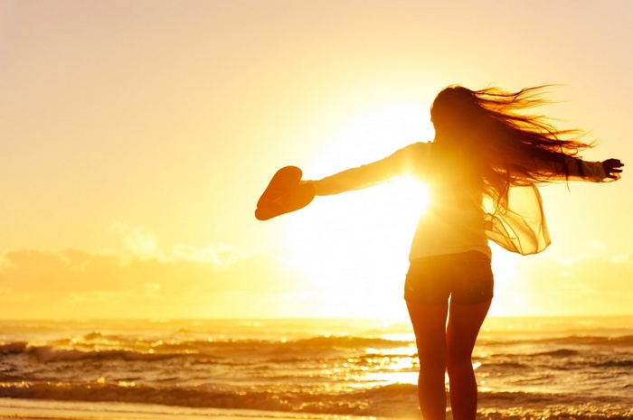 Woman with arms outstretched on a beach at sunset