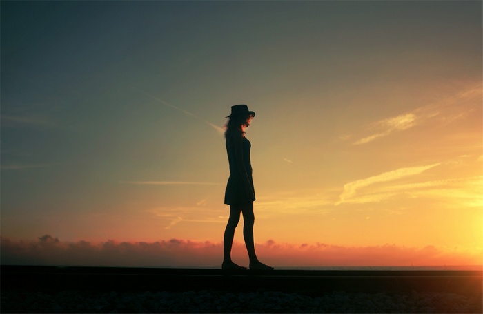 Woman in hat walking on train tracks at sunset