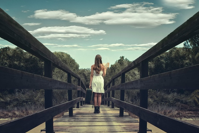 Woman with suitcase and book on a wooden bridge