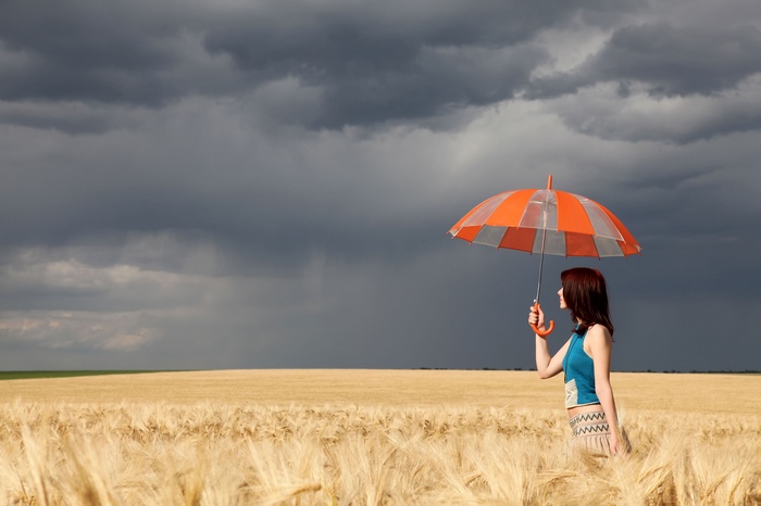 Woman with umbrella in a wheat field under stormy clouds