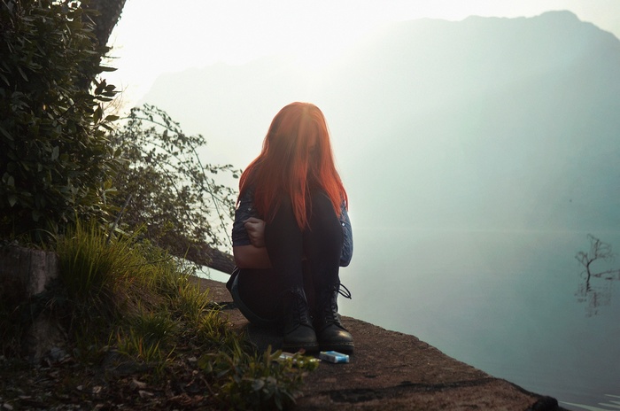 Redhead woman sitting on a cliff overlooking a lake