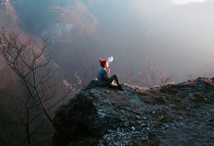 Woman with red hair smoking on a mountain cliff