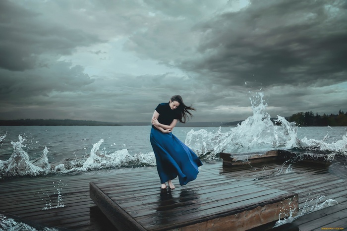 Woman in blue skirt on a pier with waves crashing